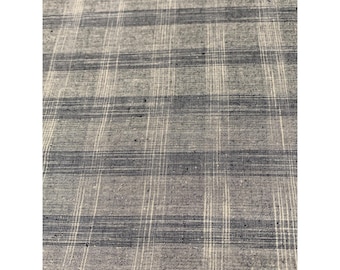 May include: Close-up of a fabric with a plaid pattern. The fabric has a gray base with dark blue and white stripes creating a grid-like design. The texture appears slightly rough, suggesting a natural fiber.