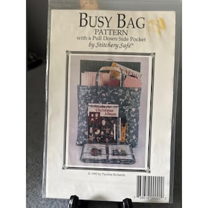 Może przedstawiać: Wzór Busy Bag firmy Stitchery Safe, z kieszenią boczną z klapką. Obraz przedstawia torbę z kwiatowym wzorem, zawierającą album świąteczny, tkaninę i inne materiały do szycia. Wzór pochodzi z 1992 roku.