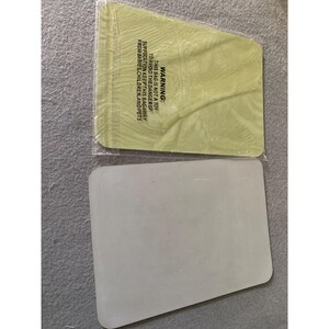 May include: Two rectangular, light-colored objects. One is a pale green, sealed in clear plastic, with a warning label. The other is a solid, off-white rectangle. The warning label text reads: "WARNING: THIS BAG IS NOT A TOY TO AVOID THE DANGER OF SUFFOCATION KEEP THIS BAG AWAY FROM BABIES, CHILDREN, AND PETS."