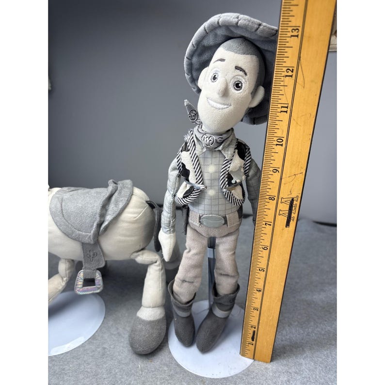 K&ouml;nnte beinhalten: Pl&uuml;sch-Cowboy-Puppe mit passendem Pferd. Die Cowboy-Puppe tr&auml;gt einen grauen Hut, eine Weste und Stiefel. Das Pferd hat einen grauen Sattel. Ein Holzlineal liegt neben der Puppe und misst etwa 33 cm.