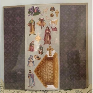 May include: A sheet of Christmas-themed stickers featuring religious figures, angels, and decorative elements. The stickers include images of the nativity scene, a cross, and other festive symbols. The background is a dark purple with a repeating pattern.