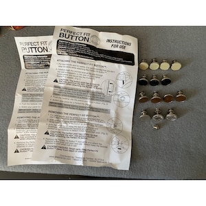 May include: A close-up of a pack of Perfect Fit Buttons, a product for attaching buttons to clothing. The pack includes instructions for attaching and removing the buttons. The buttons are silver and come in various sizes.