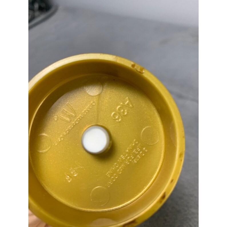 K&ouml;nnte beinhalten: Ein goldfarbener Plastikdeckel mit einem wei&szlig;en Aufkleber in der Mitte. Der Deckel tr&auml;gt die Aufschrift "489" und "W".