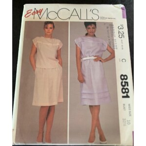 May include: A vintage McCall's sewing pattern featuring two women modeling different outfits. The pattern includes a skirt and top set and a dress with a belt. The pattern number is 8581.