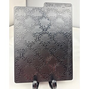 Op de afbeelding: Een rechthoekige zwarte Sizzix embossing folder met een herhalend ogee-patroon met gedetailleerde ranken en bladeren. Het plastic gereedschap heeft een getextureerd oppervlak en bevat de merknaam Sizzix in reliëf aan de bovenste middenrand.