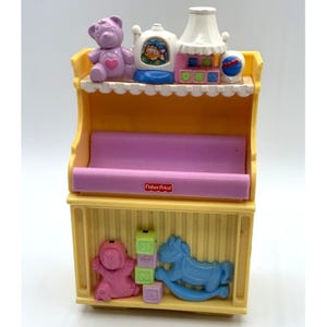 May include: A yellow and pink Fisher-Price toy shelf with a variety of colorful toys. The shelf features a purple teddy bear, a white lamp, and a blue rocking horse. The toy shelf has a pink shelf and a yellow base.