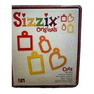 May include: A Sizzix Originals die-cut set featuring various charm and frame shapes in red, orange, and yellow. The packaging includes the text "Charms, Frames" and "Cuts".