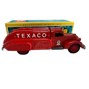 May include: A red Texaco tanker truck toy with black wheels and chrome accents. The truck has the Texaco logo in white on the side and a Texaco star logo. The truck is part of a collector's series.