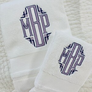 May include: Two white towels with a purple and blue monogram embroidered on them. The monogram is in a geometric pattern and reads "MRP".