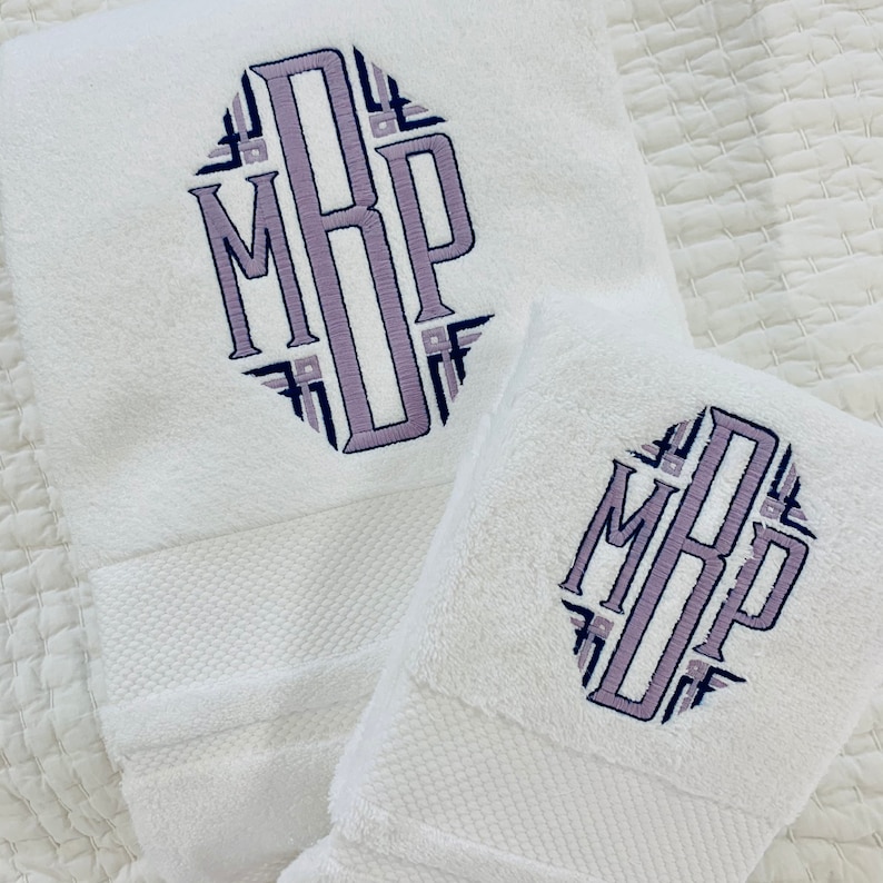 May include: Two white towels with a purple and blue monogram embroidered on them. The monogram is in a geometric pattern and reads "MRP".