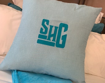 Może przedstawiać: Poduszka w niebiesko-białe paski z wyszytym monogramem "SHG" w kolorze turkusowym.