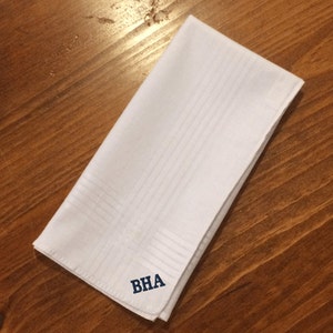 May include: White linen pocket square with a blue embroidered monogram "BHA".