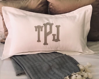 Op de afbeelding: Een wit kussen met een grijs geborduurd monogram "TPJ" op een bed met een grijs en wit dekbed.