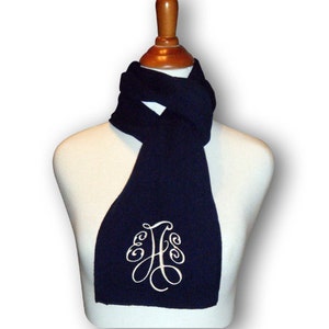 May include: A navy blue fleece scarf with a white embroidered monogram. The monogram is a stylized letter "H" with decorative flourishes.