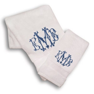 May include: Two white towels with blue embroidered monograms. The monogram is a stylized "EMB" with a decorative flourish.