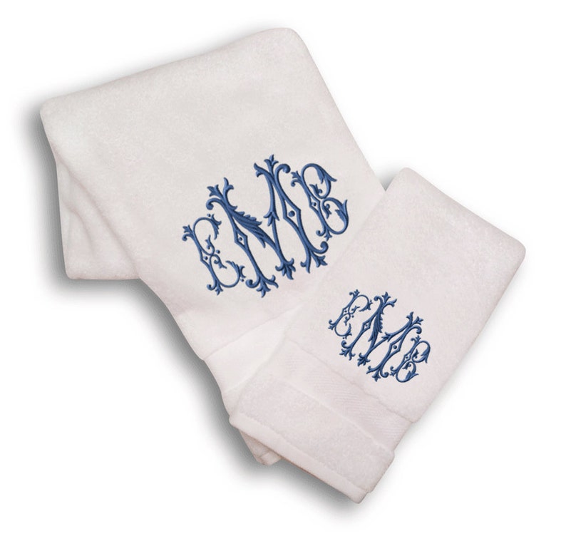 May include: Two white towels with blue embroidered monograms. The monogram is a stylized "EMB" with a decorative flourish.