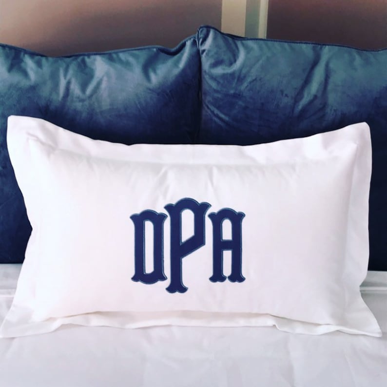 May include: White pillow with a navy blue monogram of the letters "DPA" in a decorative font.