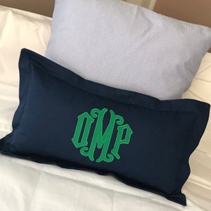 May include: A navy blue pillow with a green monogram of the letters "OMP" in a decorative font.