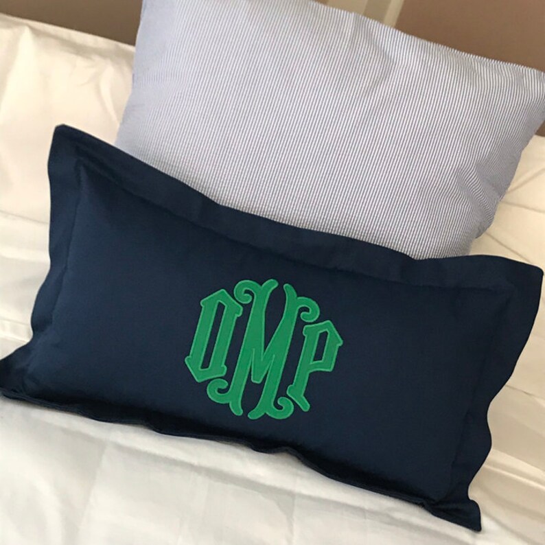 May include: A navy blue pillow with a green monogram of the letters "OMP" in a decorative font.
