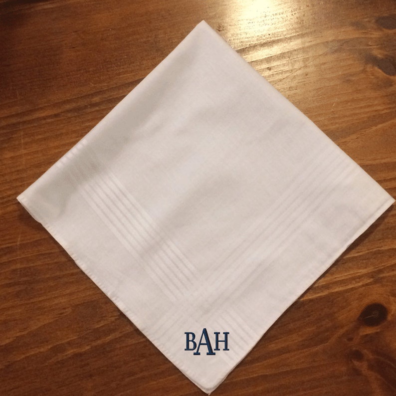 May include: White cotton handkerchief with a navy blue embroidered monogram "BAH" in the center.