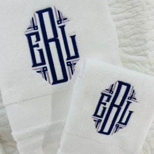 May include: Two white towels with a navy blue and light purple monogram of the letters "EBL" embroidered on each towel.