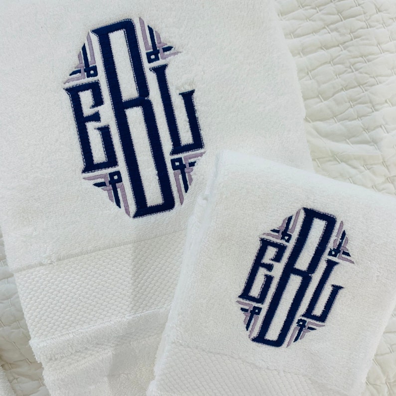 May include: Two white towels with a navy blue and light purple monogram of the letters "EBL" embroidered on each towel.