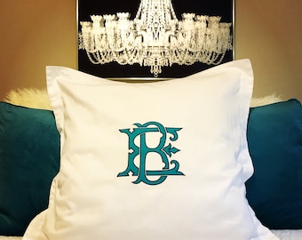 May include: White pillowcase with a teal monogram of the letters "B" and "E". The pillow is on a bed with teal pillows and a black and white chandelier print in the background.