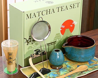 May include: Matcha tea set in a box with a Japanese landscape design. The set includes a bamboo whisk, a ceramic bowl, a scoop, a sifter, a small ceramic vase, and a bamboo spoon. The bowl is blue and red, and the box says "Matcha Tea Set".