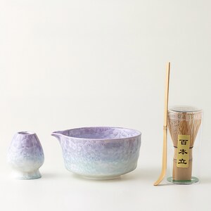 May include: A matcha tea set featuring a textured, lavender and blue ceramic bowl, a whisk, a whisk holder, and a small ceramic whisk stand. Ideal for preparing traditional Japanese matcha tea.