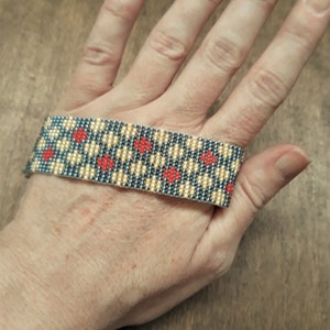 Peut inclure: Un bracelet en perles avec un motif g&eacute;om&eacute;trique dans les tons de gris, beige et rouge.