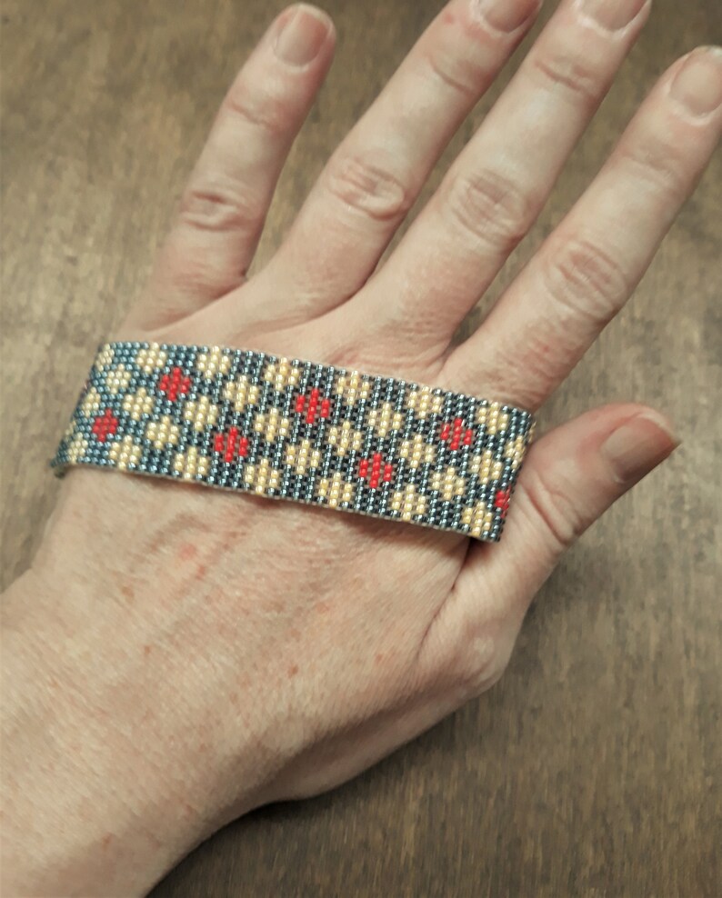 Peut inclure: Un bracelet en perles avec un motif g&eacute;om&eacute;trique dans les tons de gris, beige et rouge.