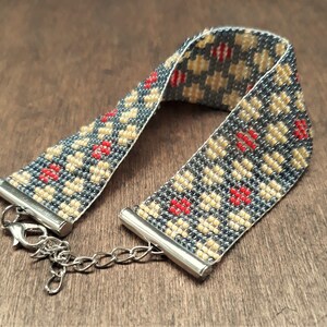 Peut inclure: Un bracelet en perles avec un motif g&eacute;om&eacute;trique dans les tons de gris, beige et rouge. Le bracelet a un fermoir argent&eacute;.