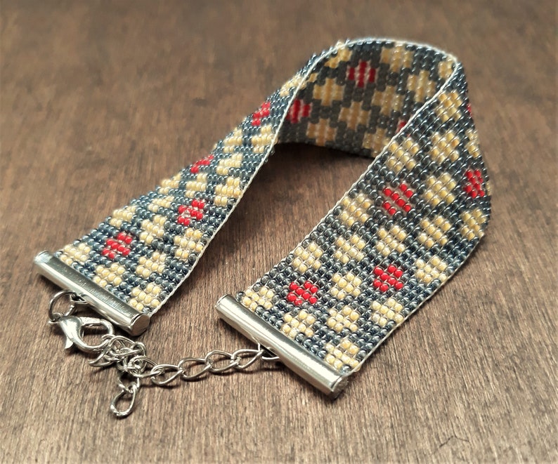 Peut inclure: Un bracelet en perles avec un motif g&eacute;om&eacute;trique dans les tons de gris, beige et rouge. Le bracelet a un fermoir argent&eacute;.