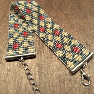 Peut inclure: Un bracelet en perles avec un motif g&eacute;om&eacute;trique dans les tons de gris, beige et rouge. Le bracelet a un fermoir et une cha&icirc;ne argent&eacute;s.