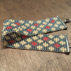 Peut inclure: Un bracelet en perles avec un motif g&eacute;om&eacute;trique de perles grises, beiges et rouges. Le bracelet est dot&eacute; de fermoirs en m&eacute;tal argent&eacute;.