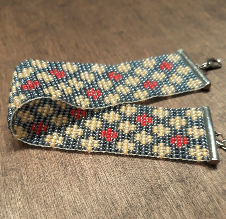 Peut inclure: Un bracelet en perles avec un motif g&eacute;om&eacute;trique de perles grises, beiges et rouges. Le bracelet est dot&eacute; de fermoirs en m&eacute;tal argent&eacute;.