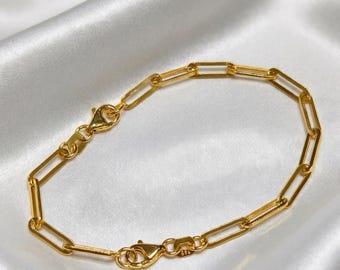 May include: A gold-toned chain bracelet featuring elongated rectangular paperclip-style links. The bracelet is secured with a polished lobster claw clasp and includes a small rectangular tag near the closure mechanism.