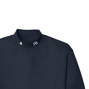 May include: Navy blue long-sleeve mock turtleneck shirt. The shirt features a small white logo on the collar. The shirt has a classic, simple design, with long sleeves and a mock turtleneck collar.