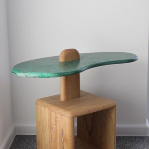 May include: A wooden side table with a green, irregularly shaped top and a lower shelf. The table is made of natural wood with a rustic finish.