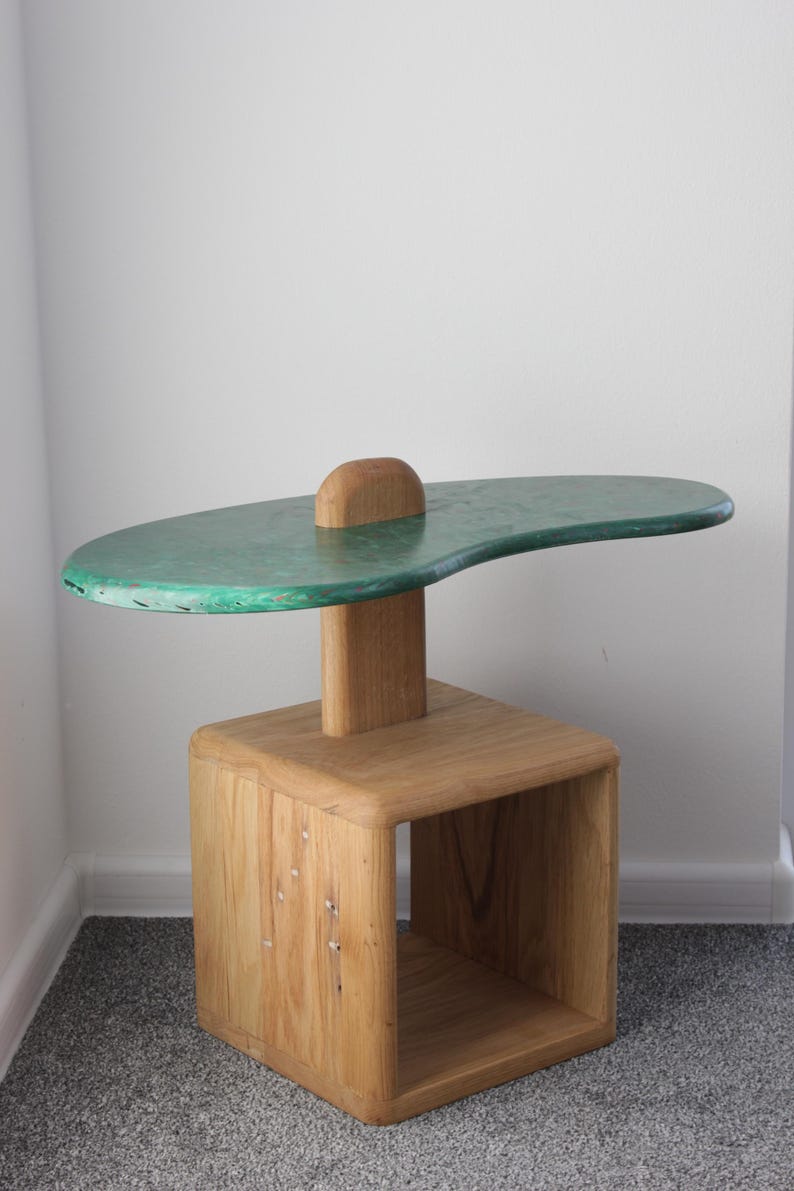 May include: A wooden side table with a green, irregularly shaped top and a lower shelf. The table is made of natural wood with a rustic finish.