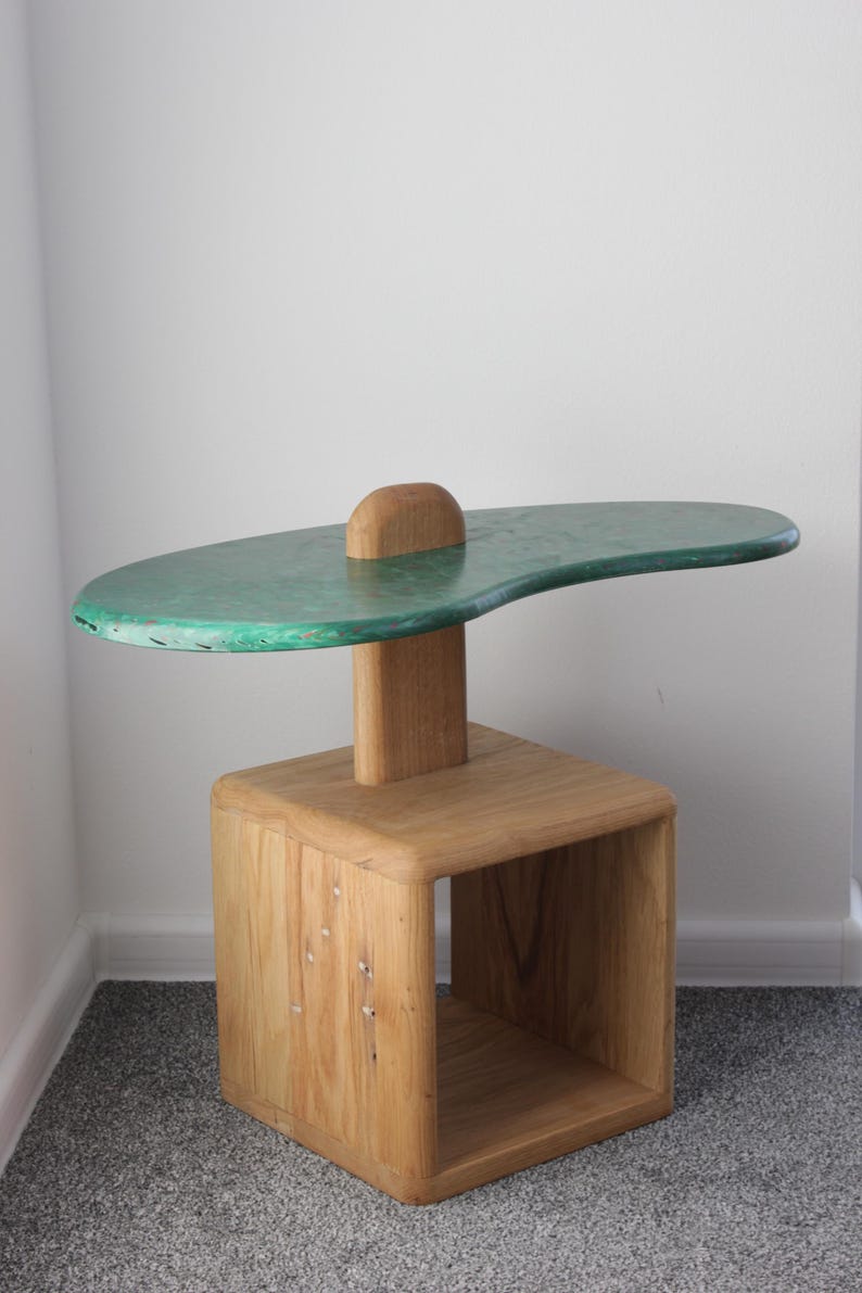 May include: A unique side table with a green, organic-shaped top and a wooden base with a shelf. The table is made of wood and has a rustic, handmade look.