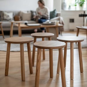 Puede incluir: Cuatro taburetes de madera con asientos redondos y tres patas anguladas cada uno. Los taburetes son de madera de color claro y están dispuestos en una habitación con una paleta de colores neutros. Diseño simple y minimalista.