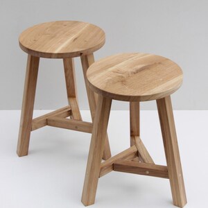 May include: Two wooden stools with round seats and three angled legs. The stools are made of light-colored wood and have a natural finish. The seats are approximately 12 inches in diameter.
