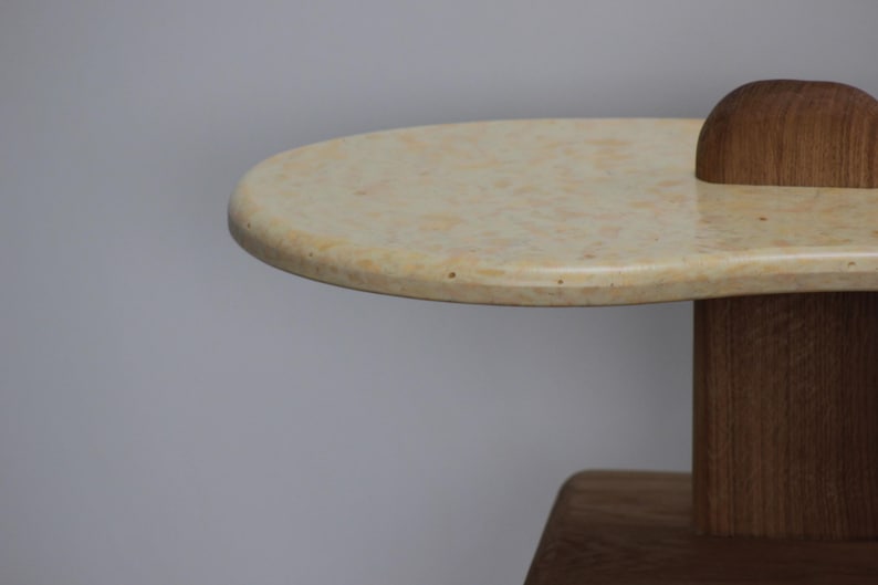 May include: Close-up of a light beige oval table top with a wood base. The table top has a speckled texture.