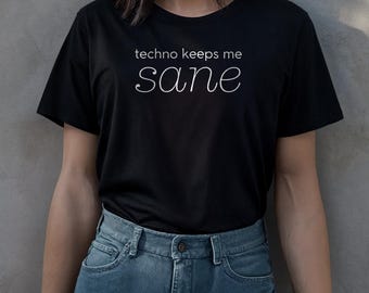 May include: Black t-shirt with the white text "techno keeps me sane" in a handwritten style font. The shirt is paired with blue denim jeans. The overall style is casual and comfortable.