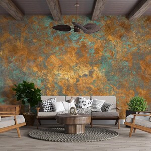May include: A living room with a copper-colored textured wall, a ceiling fan, and wooden beams. The room features a light-colored sofa with decorative pillows, wooden chairs, and a round coffee table. Plants and a rug complete the decor.