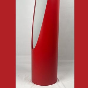 May include: A tall, cylindrical red object with a curved, open section revealing a white interior. The object has a smooth, matte finish and stands upright against a white background. The design is minimalist and modern.