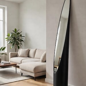 Puede incluir: Un espejo de pie alto, negro y de forma ovalada se apoya contra una pared de color neutro. El espejo tiene un diseño elegante y moderno y refleja el interior de la habitación, incluyendo un sofá seccional beige, una mesa de centro y una gran planta en maceta. El espejo mide unos 178 cm de alto.