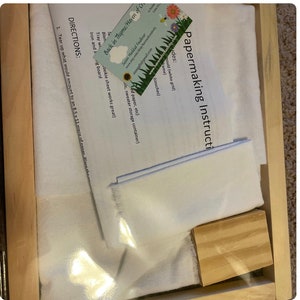 May include: Papermaking instruction kit with instructions, white fabric, and a wooden block. The kit includes a business card with contact information and a website address. The instructions are printed on white paper.
