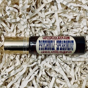 Puede incluir: Un frasco de vidrio marrón con rodillo y tapa dorada. La etiqueta dice "GIFTEDCHICKEN.COM PATCHOULI SPEARMINT ALMOND OIL, PATCHOULI SPEARMINT BOSS"